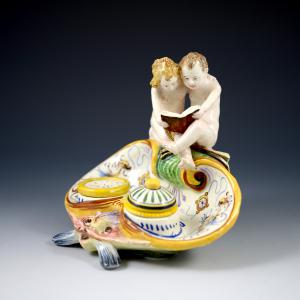 Calamaio a forma di razza che sorregge due putti in lettura